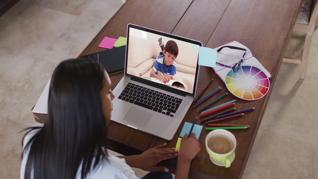 maestra caucásica usando una computadora portátil en videollamada con un escolar, tomando notas