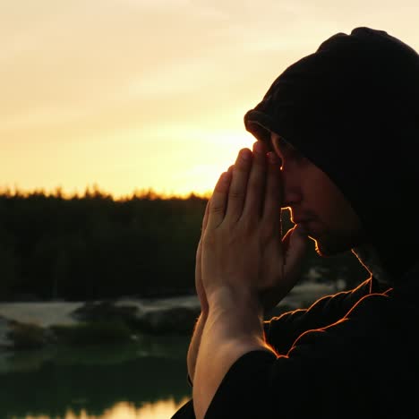 a young man in a hood prays at sunset 3