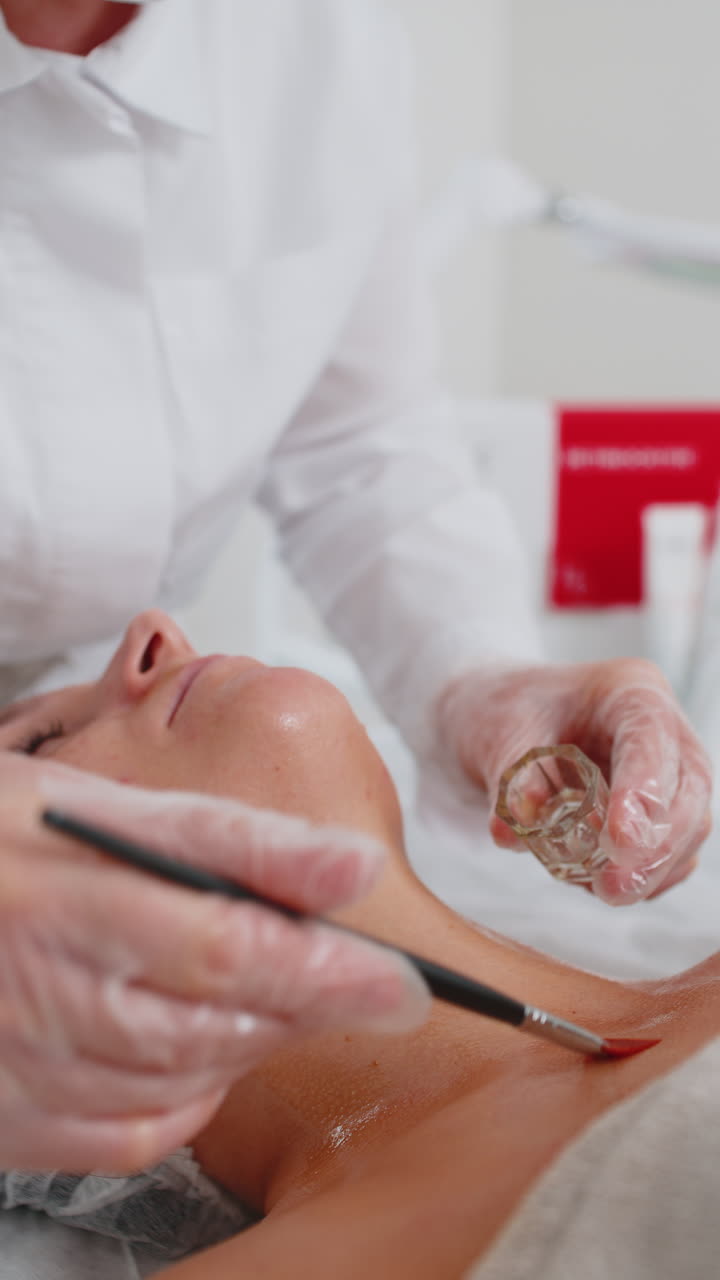 Terapia enzimatica: estetista che applica una crema medica idratante sul petto di una giovane donna con un pennello