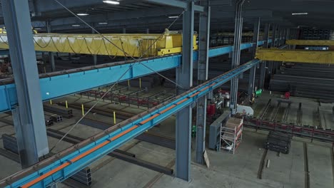 Panoramic-aerial-pullback-orbit-around-overhead-bridge-crane-in-steel-beam-warehouse