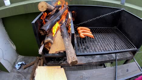 video of a white man putting sausages on a black grill with burning fire on a sunny day