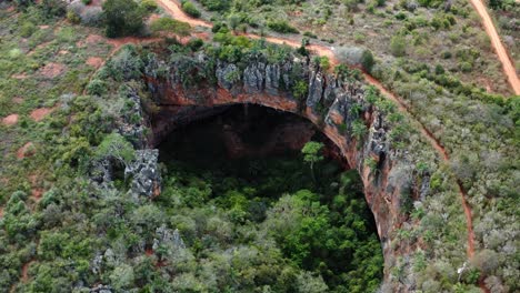 Plano-Medio-De-Un-Dron-Aéreo-De-La-Gran-Entrada-De-La-Cueva-Lapa-Doce-De-Rocas-Coloridas-Con-Una-Selva-Tropical-Autónoma-Debajo-En-El-Parque-Nacional-Chapada-Diamantina-En-Bahia,-Noreste-De-Brasil