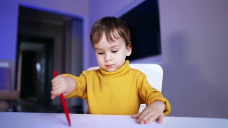 focused baby boy drawing on the paper with a red pen. lovely toddler learning to use felt pen at home.