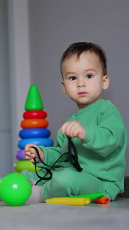 caucasian baby sitting on the floor at the yellow toy box. beautiful child playing with a black lace. vertical video