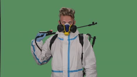 retrato de un hombre joven con un traje de protección, gafas de seguridad, guantes y un respirador con un desinfectante de alta presión mira con confianza a la cámara. pantalla verde, llave de croma. cámara lenta. primer plano