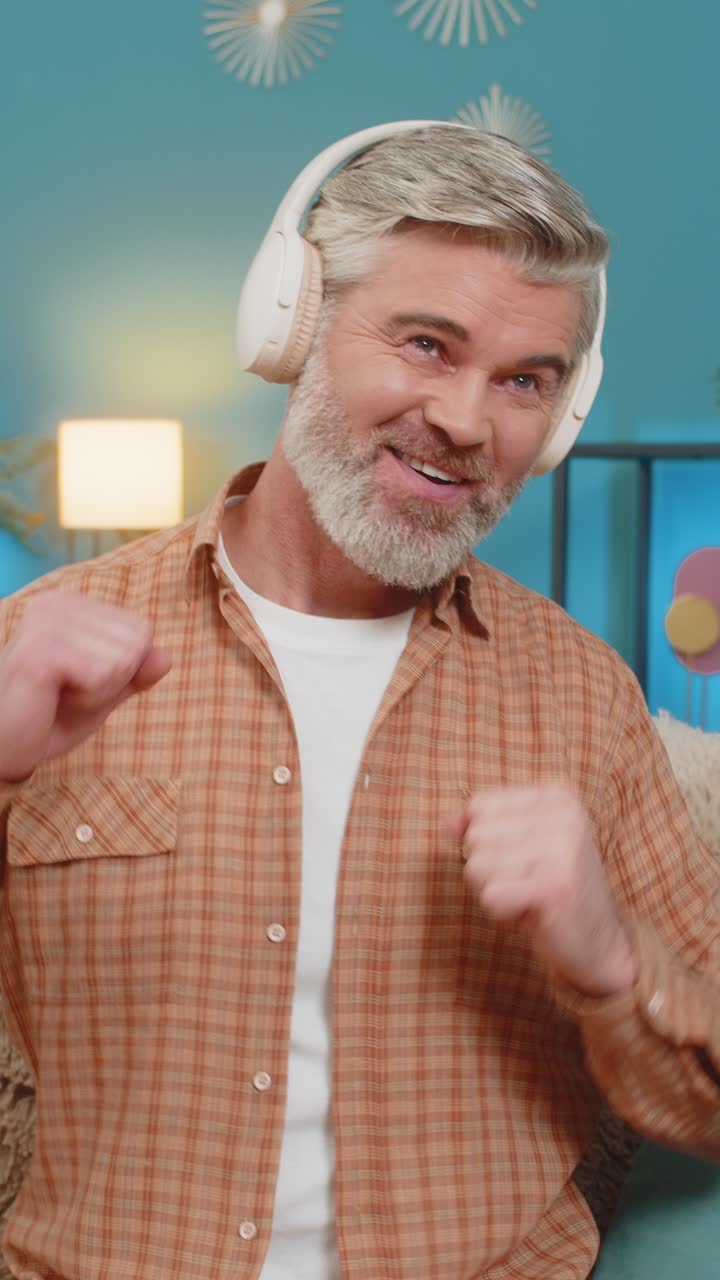 Uomo maturo che si rilassa sul divano con le cuffie wireless godendosi la musica e ballando a casa