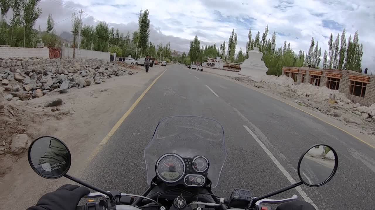 A bumpy bike ride on a well build Himalayan village road with Mountain ranges visible at a distance. Shot from biker’s point of view.