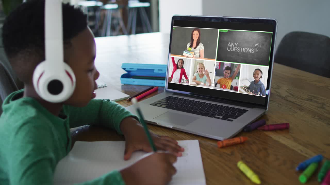 Schoolboy using laptop for online lesson at home, with diverse teacher and class on screen