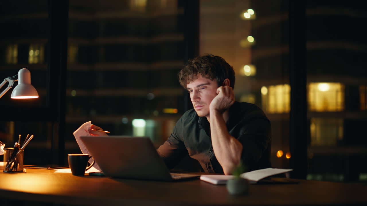 Dipendente che lavora fino a tardi, utilizza il portatile e legge documenti di notte in ufficio. Manager stanco