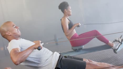 diverse group fitness class training hard on rowing machines at gym, in slow motion