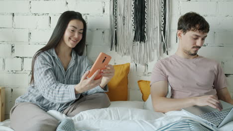 couple in bed, taking selfie and working on laptop