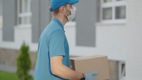 a delivery man wearing a protective mask and gloves passes the parcel to the customer and receives a contactless payment via nfc