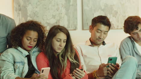 group of friends sitting on sofa and looking at phone screen