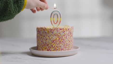 studio shot birthday cake covered with decorations and candle in shape of number 0 being lit and blown out