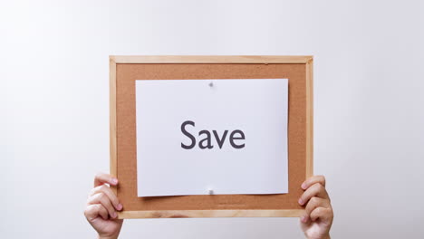 Woman's-hand-shows-the-paper-on-board-with-the-word-Save-in-white-studio-background-with-copy-space