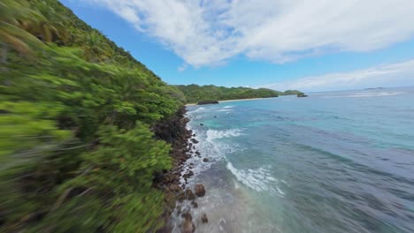 Drone-FPV-Avanza-Sobre-La-Costa-Rocosa-Hasta-Una-Remota-Playa-De-Arena-Tropical