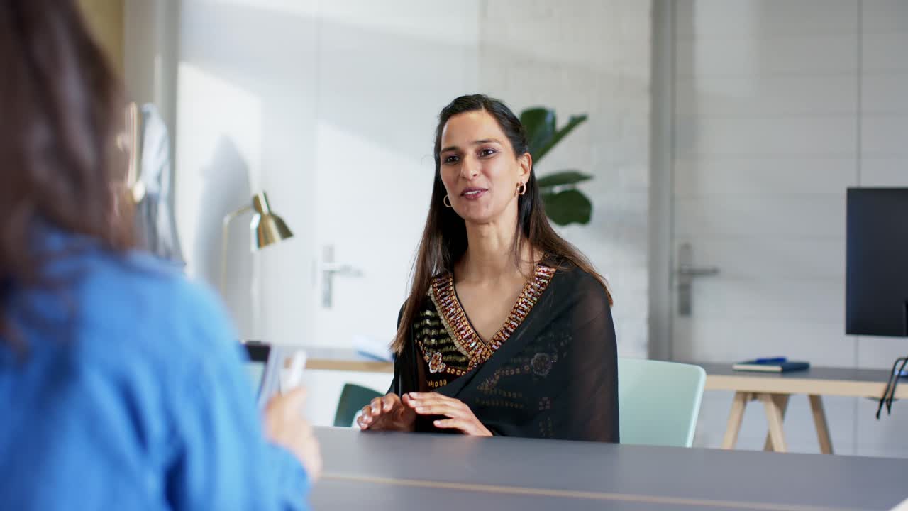 Indian woman greeting interviewer laughing at joke while nodding and explaining at conference table