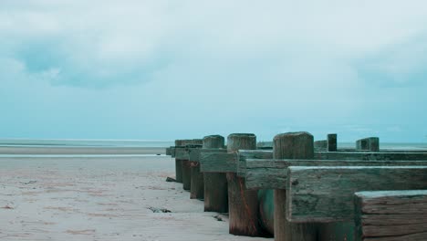 Eine-Kleine-Holzkonstruktion-Streckt-Sich-In-Richtung-Ozean,-Während-Der-Ausgetrocknete-Strand-Bei-Ebbe-Schweigend-Daliegt,-Während-Sich-Am-Fernen-Horizont-Wütende-Stürme-Bilden