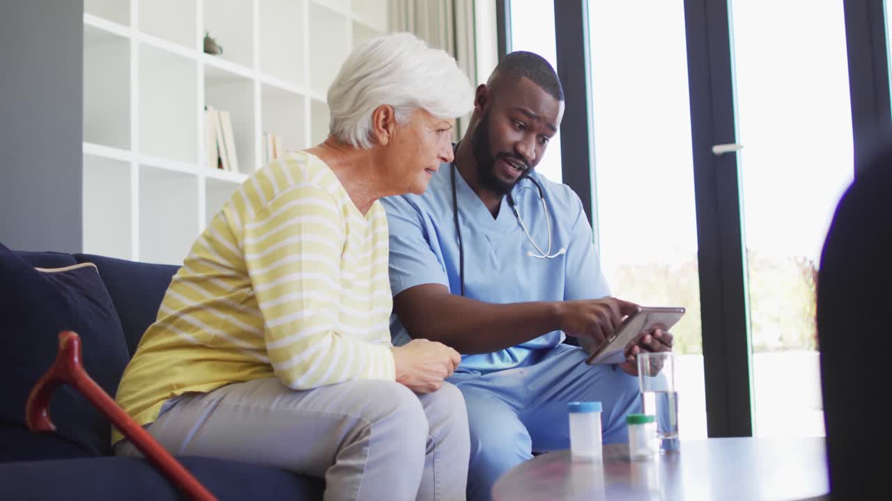 Video of african american male doctor using tablet with caucasian senior woman