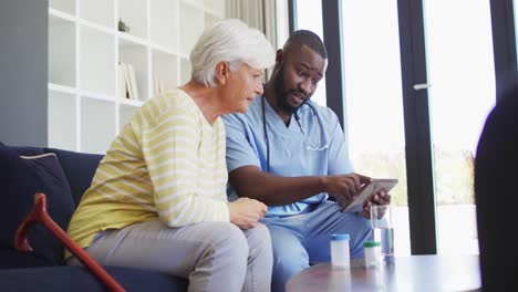 Video-Eines-Afroamerikanischen-Arztes,-Der-Ein-Tablet-Mit-Einer-Kaukasischen-Seniorin-Verwendet