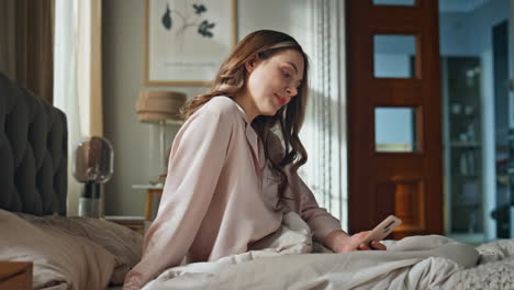 woman in pajamas sitting on bed using a smartphone