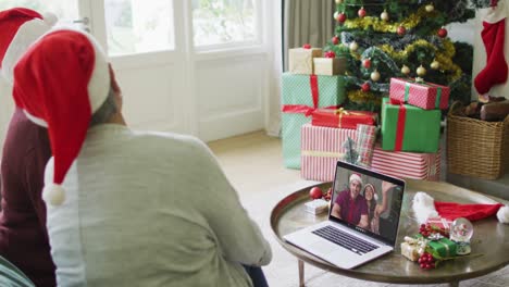 Two-senior-diverse-female-friends-using-laptop-for-christmas-video-call-with-couple-on-screen