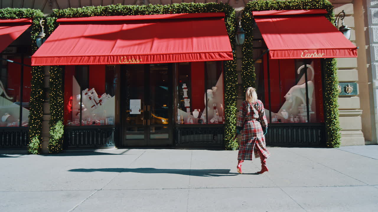 New York, VS, 5 oktober 2025: Vrouw loopt langs luxe juwelierszaak met rode luifels. Vrouw in geruite jas wandelt over trottoir langs luxe etalage met rode feestversieringen in NYC.