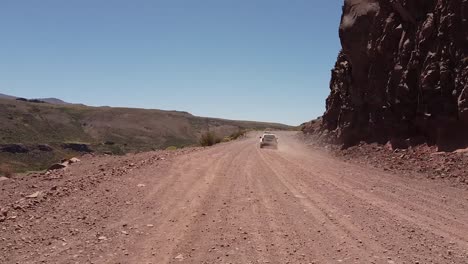 White-colored-car-is-passing-on-the-road-leading-through-natural-landscape-during-sunshine-day,-aerial-recorded-in-the-mountains-of-Patagonia,-Argentina,-South-America