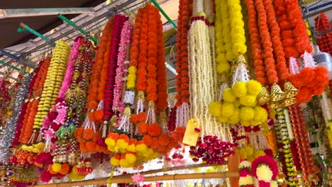 brightly colored flower garlands hang in a bustling singapore market stall, with vibrant marigold, jasmine, and rose strands under natural daylight, slight camera pan