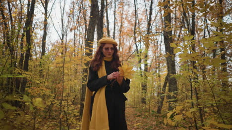 stylish lady in a yellow beret and long black coat strolls through a dense autumn forest, holding vibrant yellow leaves, creating a picturesque autumnal scene