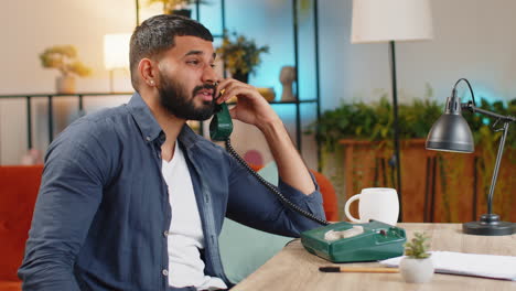 tired indian man freelancer talking on retro wired telephone annoyed boring conversation at office