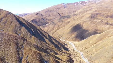 aerial over cars traveling on a road through dry mountain landscape in the south island of new zealand