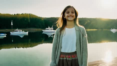 a young girl smiles while standing on a dock by a lake with boats in the background