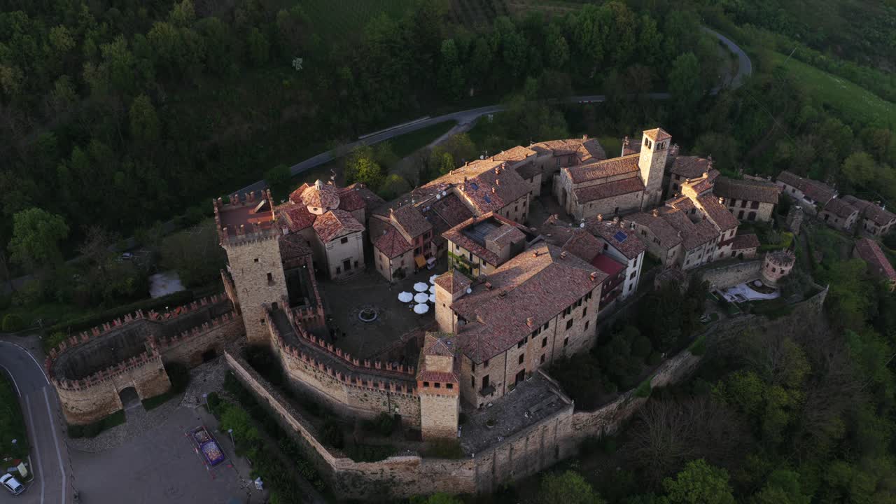 Aerial drone shot revealing the impressive medieval Vigoleno castle and its fortified village nestled in the green hills of Emilia-Romagna at sunset, Italy