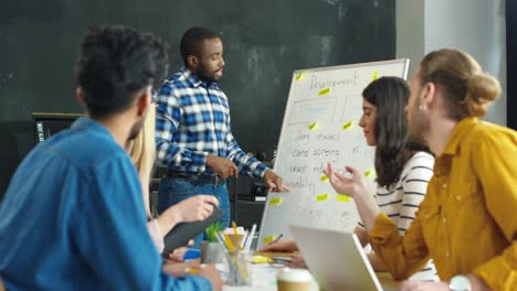 junger mann, der beim startup-meeting 1 mit seinen kollegen über die entwicklungsstrategie spricht und darüber berichtet