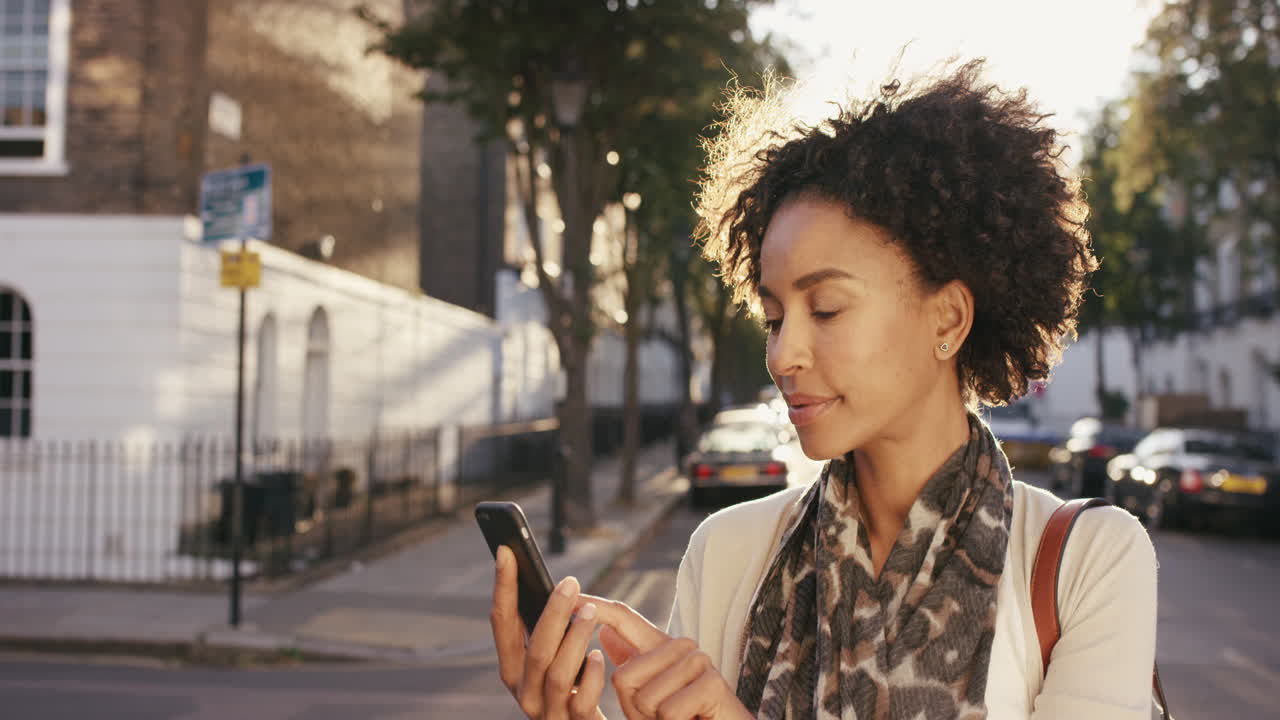 Beautiful Mixed race woman using smart phone technology app walking through city