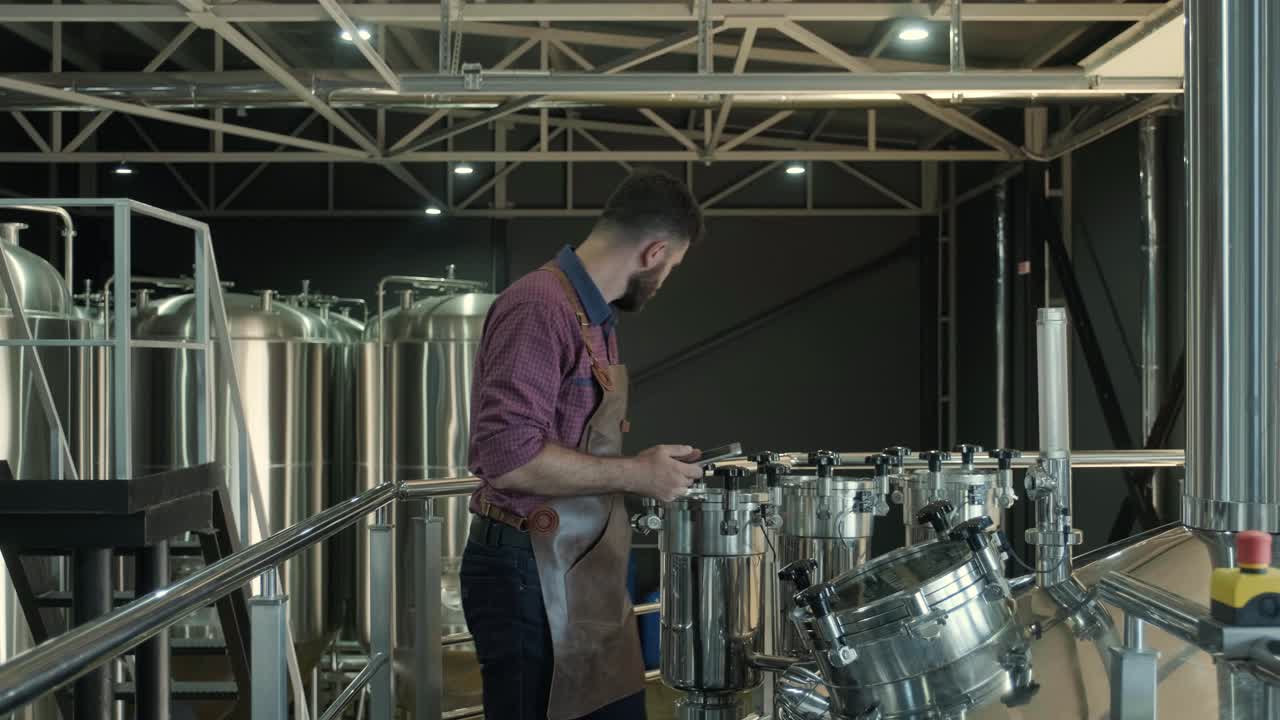 un joven cervecero con un delantal de cuero supervisa el proceso de fermentación de la cerveza en una fábrica de cerveza moderna