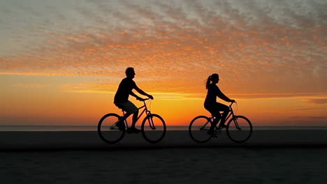 silhouetted couple biking at sunset on the beach