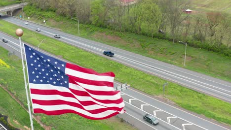 aerial of american flag waving in breeze about highway traffic