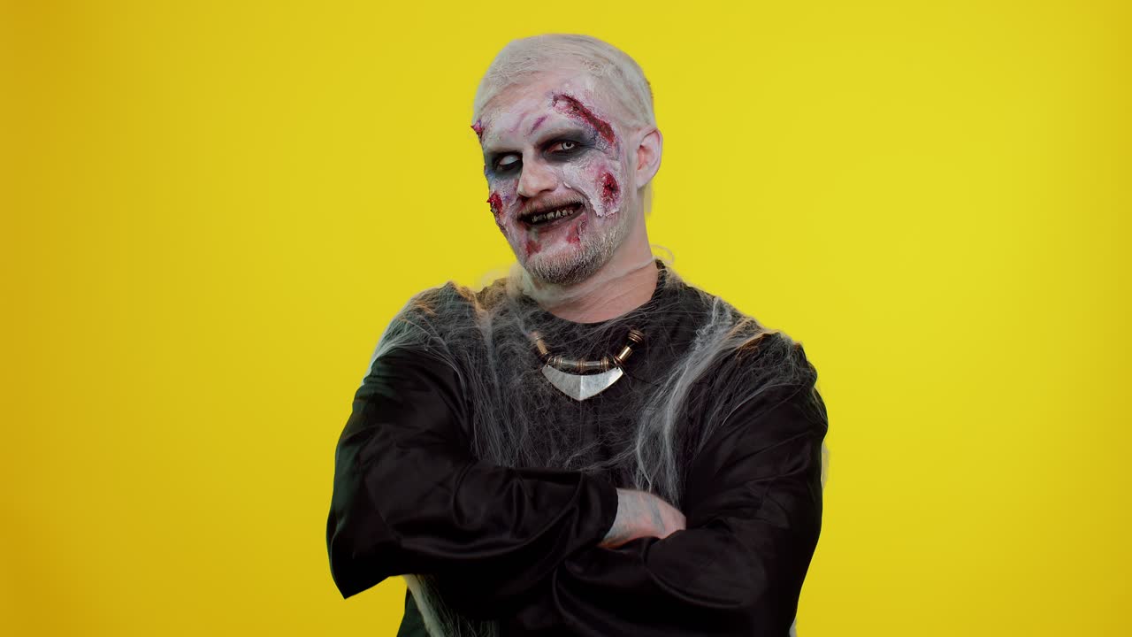 hombre espeluznante alegre halloween zombie haciendo caras, mira a la cámara, sonríe terriblemente con los dientes sucios