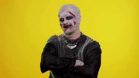 cheerful creepy man halloween zombie making faces, looks at camera, smiles terribly with dirty teeth