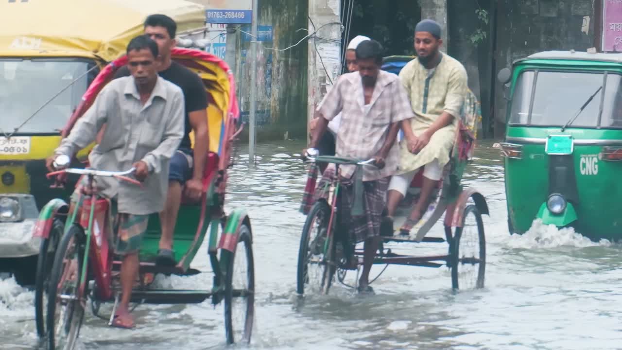 Bangladesh cycling taxi bikes transporting people through flooded downtown Sylhet city street