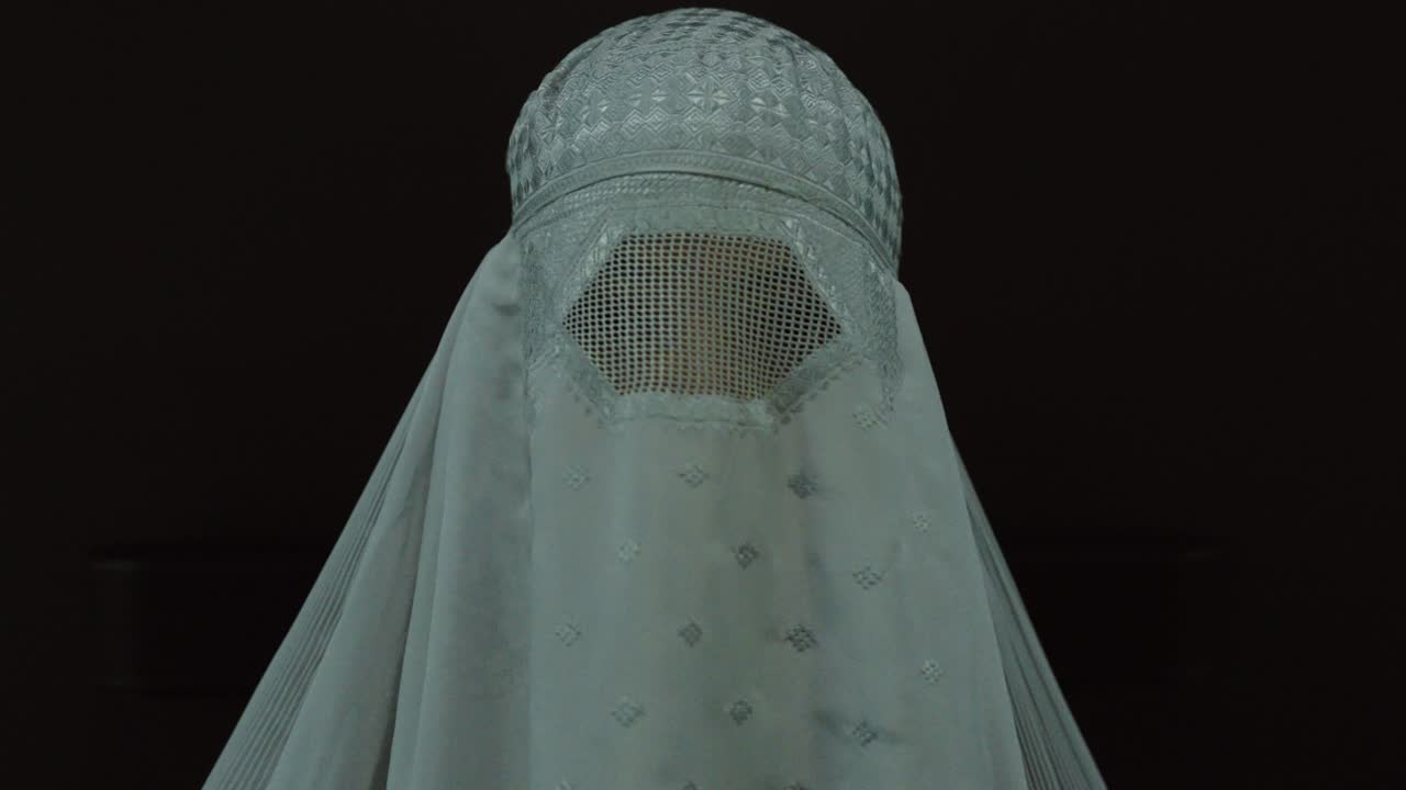 A woman covered in traditional Muslim clothing poses for a portrait against a dark background while the camera slowly moves backward from the front