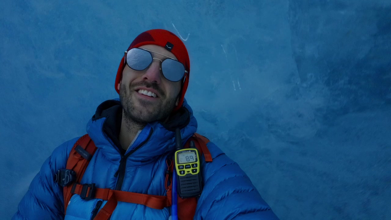 Escursionista uomo con occhiali da sole e abbigliamento invernale si muove lungo una parete di ghiaccio blu all'interno del Ghiacciaio del Morteratsch, scatto ravvicinato di viaggio avventura