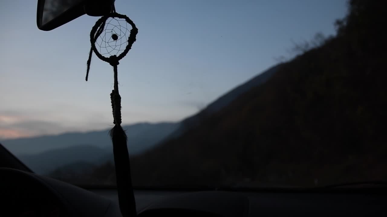 hermoso atrapasueños hecho a mano moviéndose dentro de un camión en una carretera de montaña al atardecer