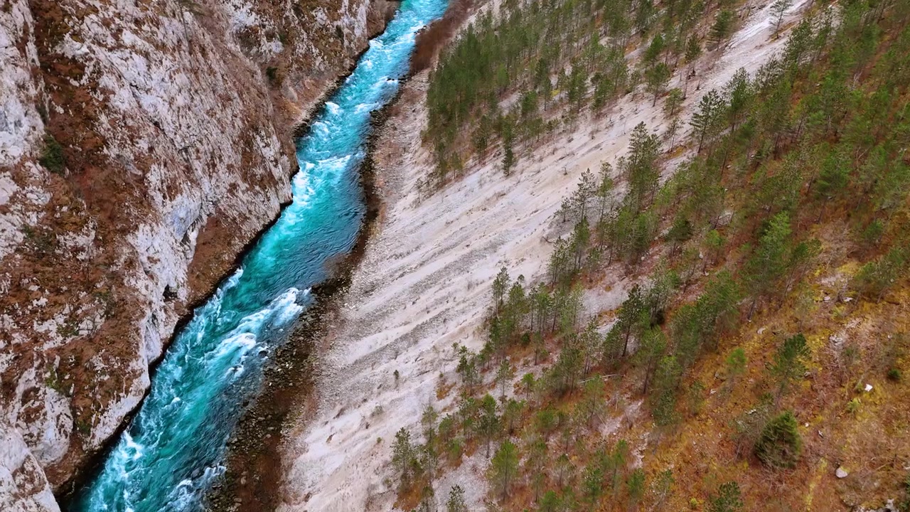 Vista aerea di un fiume turchese con pini e una parete di scogliera calcarea. L'acqua turchese scorre tra una ripida parete calcarea sulla sinistra e un pendio roccioso con pini sparsi sulla destra.