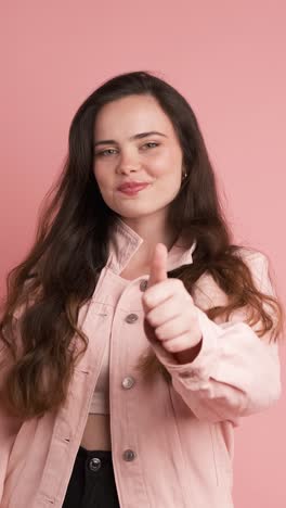 happy young woman showing thumbs up in pink studio