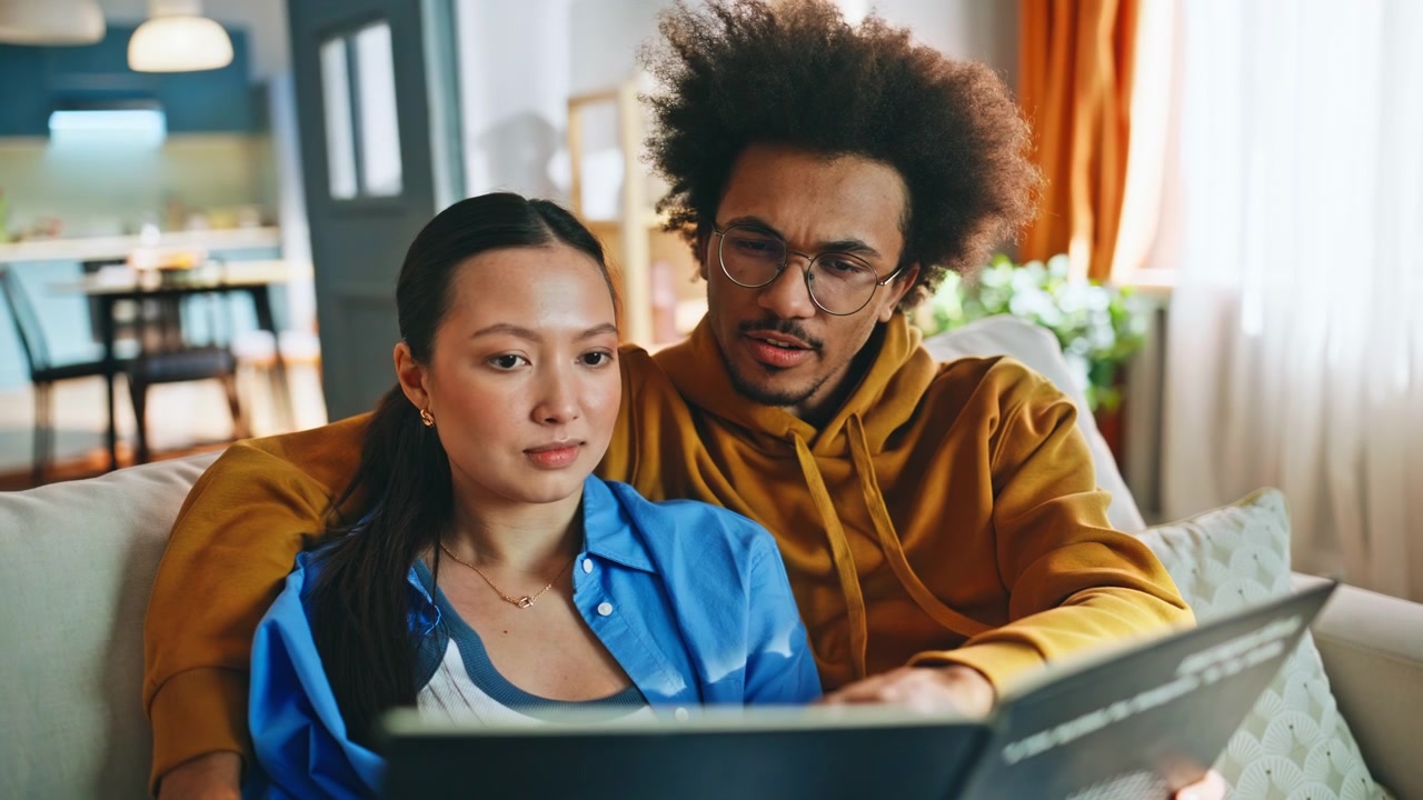 Multiethnic couple browsing photo album on home sofa. Closeup nostalgic memories