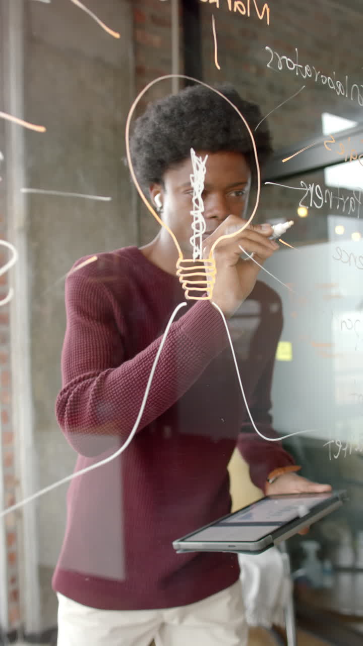 Vertical video of african american man taking notes on glassboard at home, slow motion