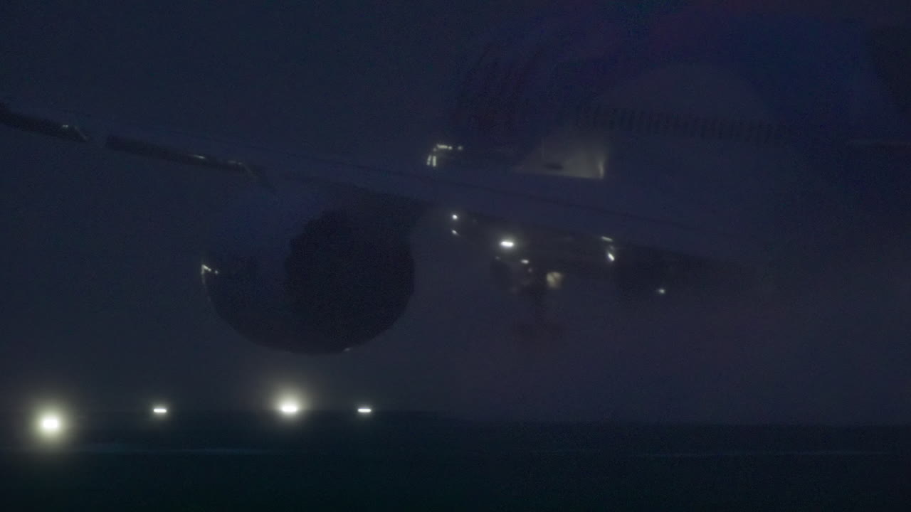 Motore e ala di un aereo commerciale in rullaggio su pista nebbiosa di notte
